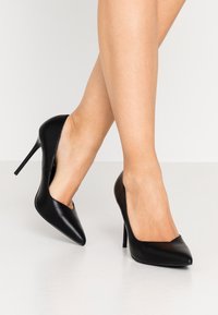 Schwarze Leder-High Heels mit einer spitzen Zehenpartie und einem schlanken, minimalistischen Design. Die Schuhe verfügen über ein ausgeschnittenes Seitendetail und einen Stiletto-Absatz.