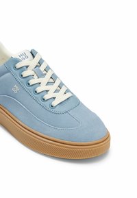 Baskets en daim bleu clair avec lacets blancs, semelle en caoutchouc couleur gomme, et logo "HUGO" sur le côté et la languette, vues en légère inclinaison latérale.