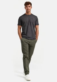 Camiseta de manga corta gris oscuro con un bolsillo en el pecho, combinada con pantalones verde oliva y zapatillas blancas. Tejido suave y corte casual.