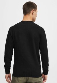 Black knit sweater with a round neckline and ribbed cuffs. Features a textured fabric and raglan sleeve design. Classic, versatile fit.