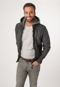 Giacca di pelle nera con fodera in felpa grigia, chiusura con zip e tasche laterali. Indossata sopra una t-shirt grigia chiara e abbinata a jeans grigi.