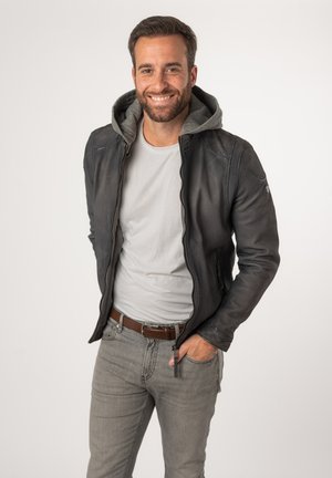 Schwarze Lederjacke mit grauem Kapuzenfutter, Reißverschlussfront und seitlichen Taschen. Getragen über einem hellgrauen T-Shirt und kombiniert mit grauen Jeans.