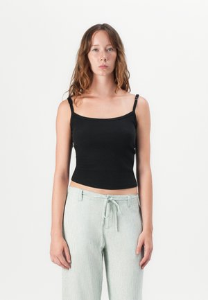 Black ribbed tank top with thin straps, fitted design, and a scooped neckline, paired with light green striped wide-leg pants.