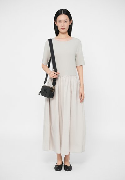 Top cinza claro com mangas curtas, combinado com uma saia longa e fluida bege. Bolsa cruzada preta com detalhes em dourado, usada com sapatilhas pretas.