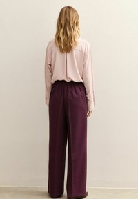 Losse blush blouse met een rechte achterkant, gecombineerd met hoog gotische, donkergroene brede broek met een elastische tailleband.