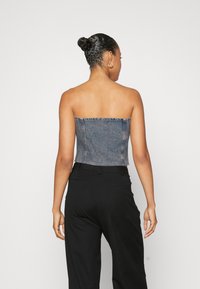 Korsett-top i denim utan axelremmar med en kortad design i ljusblå färg, med synlig sömnad och en ren, rå kant. Matchad med svarta byxor.