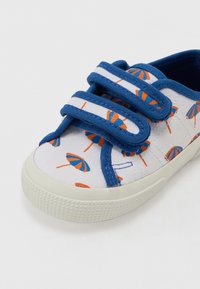Sapatilhas de tela com detalhes em azul, tiras de fecho tipo velcro, base branca com um padrão de sombrinhas laranja e azuis de praia, sola de borracha texturizada.
