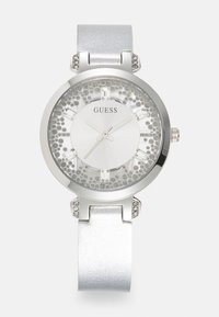 Silverfärgad damklocka med rund metallkapsel, glittrande bezel och en glittrig vit urtavla. Utrustad med en slät silverrem och kristallaccenter.