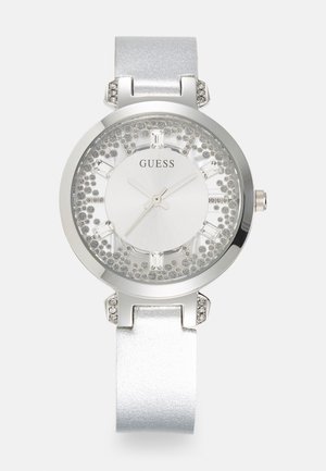 Silverfärgad damklocka med rund metallkapsel, glittrande bezel och en glittrig vit urtavla. Utrustad med en slät silverrem och kristallaccenter.