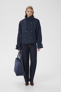 Marineblå cropped jakke med høy krage, dobbelspent design, vide ermer og store knapper. Kombinert med mørke jeans og en matchende tote.