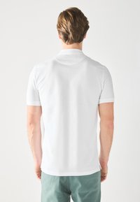 White short-sleeve polo shirt with a classic collar, smooth texture, and trim detailing on sleeve edges, worn with green shorts.