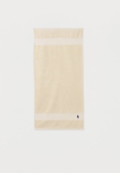 Μπεζ ορθογώνια πετσέτα με δύο πιο ανοιχτές οριζόντιες ρίγες κοντά στις άκρες και μικρό σκούρο λογότυπο στην κάτω γωνία σε λευκό φόντο.