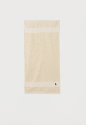 Serviette rectangulaire beige avec deux bandes horizontales plus claires près des bords et petit logo sombre dans le coin inférieur sur fond blanc.