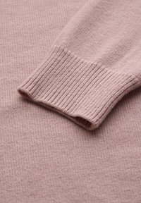 Maglione rosa chiaro con polsini a coste e un tessuto morbido e texturizzato. La vista ravvicinata mette in evidenza il motivo a maglia e i bordi puliti.