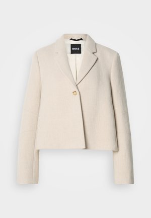 Oříznuté béžové sako s texturovaným povrchem, klopami s výřezem, zapínáním na jeden knoflík a černou značkovou štítkem uvnitř.