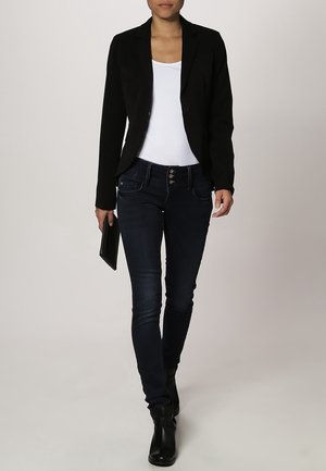 Blazer negro sobre una camiseta sin mangas blanca, combinado con jeans ajustados azul oscuro. Botines negros y un bolso de mano negro. Diseño sencillo.