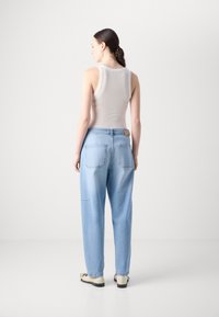 Hellgraues Tanktop kombiniert mit hellblauen, locker sitzenden Jeans, die über Gesäßtaschen und einen Lederpatch am Bund verfügen. Glatte Stofftextur.