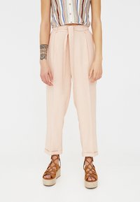 Lichte roze hoge taille broek met een strikriem, voorzien van rechte pijpen en subtiele zijnaad. Gecombineerd met bruine gespen sandaaltjes op een platform.