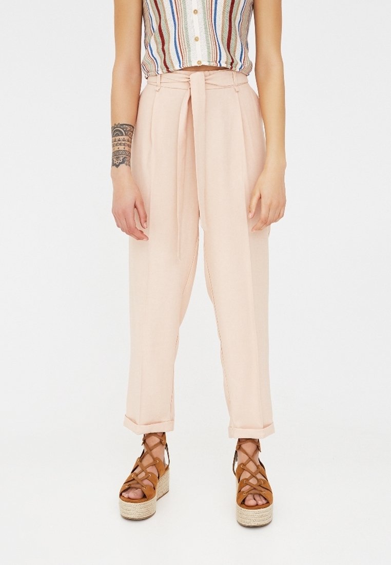 Lichte roze hoge taille broek met een strikriem, voorzien van rechte pijpen en subtiele zijnaad. Gecombineerd met bruine gespen sandaaltjes op een platform.