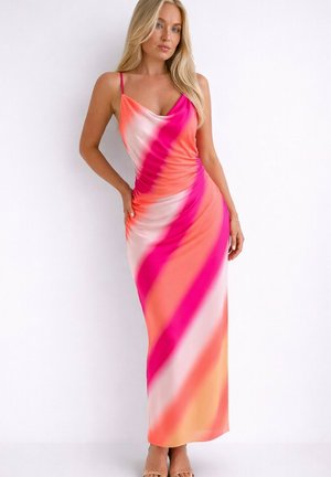 Femme debout sur fond blanc, portant une robe longue sans manches avec des rayures diagonales roses, orange et blanches.