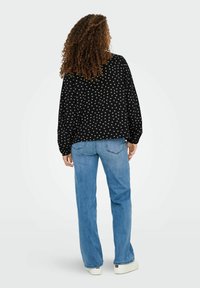 Zwarte blouse met witte bloemenprint, losse pasvorm, lange mouwen met geplooide schouders, gecombineerd met lichtblauwe flared jeans en witte sneakers.
