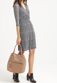 Svart och vit mönstrad klänning med V-ringning och trekvartsärmar, kombinerad med en beige läderväska med en framficka med dragkedja.