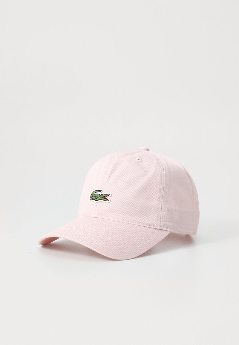 Gorra de béisbol rosa hecha de tela, con una visera curvada y un logo de cocodrilo verde bordado en la parte frontal. Textura suave.