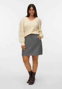 Pull en V beige avec des manches bouffantes texturées, associé à une jupe grise avec des poches latérales. Porté avec des bottines brunes.