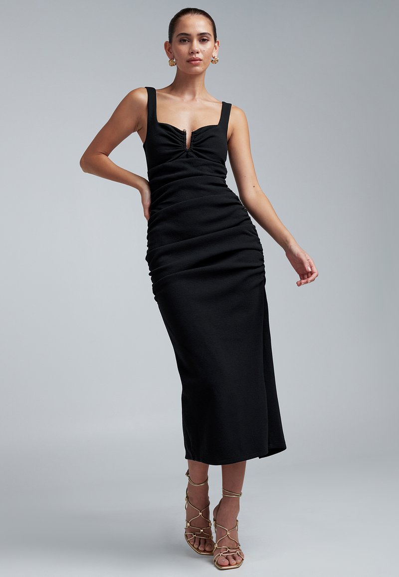 Vestido midi negro con silueta ajustada, tirantes anchos y detalle de ojo de cerradura en el escote. Tejido texturizado con costuras laterales fruncidas.