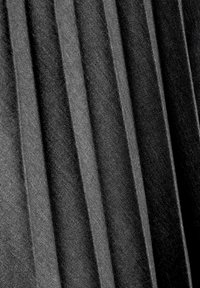 Gros plan d’un tissu plissé noir et gris foncé avec une texture visible et des plis verticaux créant des rayures ombragées.