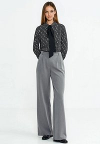 Czarna i biała bluzka w paski z wiązaniem przy dekolcie, zestawiona z szarymi spodniami o szerokich nogawkach. Gładka tkanina, dopasowany krój, prosty design.