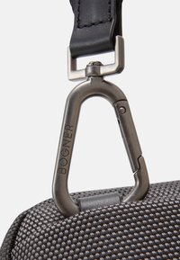 Schwarze Stofftasche mit strukturiertem Oberflächen und silbernem, metallischen Karabinerhaken, auf einer Seite mit dem eingeprägten Markennamen "BOGNER".
