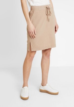 Beige katoenen rok met een trekkoord in de taille, zijzakken en een split aan de achterkant. Gecombineerd met witte sneakers met een gestructureerde zool.
