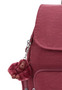 Bordeaux ryggsäck med en dragkedjeficka och en matchande fluffig gorilla nyckelring fäst på sidan.