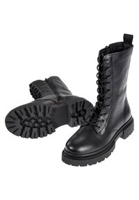 Paire de bottes noires en cuir à lacets avec fermeture éclair latérale et semelles épaisses en caoutchouc robuste, une botte debout et une botte couchée sur le côté.
