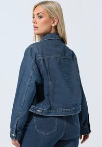 Sininen farkkutakki klassisella leikkauksella, napitus edessä sekä sivutaskut. Ominaisuuksiin kuuluu näkyvä ompelu ja hieman lyhennetty helma.