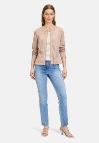 Lichtbeige suède jack met een ronde hals en rits aan de voorkant. Gepaard met lichtblauwe rechte spijkerbroeken. Eenvoudig ontwerp en neutrale kleuren.