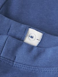 Gros plan sur une ceinture côtelée bleue avec un élastique blanc ajustable et un bouton à l'intérieur pour la personnalisation de la taille.
