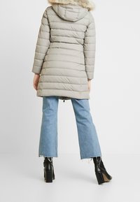 Beige, dikke winterjas met een met bont omzoomde capuchon, voorzien van horizontale quilt en een iets getailleerde Silhouet. Gecombineerd met flare jeans.