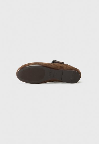 Brown suede shoe with a rounded toe, flat sole, and black hardware accent. The bottom is smooth with branding details on the outsole.