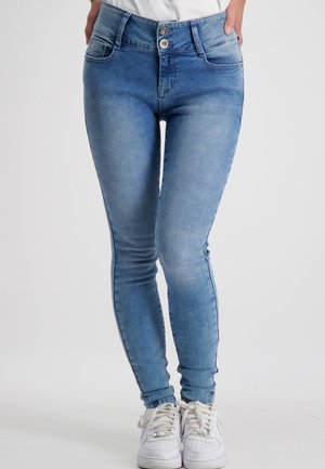 Slanke blauwe spijkerbroeken met een hoge tailleband, twee voorzakken en lichte vervaging. Gecombineerd met witte sneakers, wat een casual uitstraling geeft.