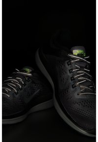 Paire de chaussures de course Nike noires avec lacets réfléchissants et étiquettes vertes "H2O REPEL" sur la languette sur fond sombre.