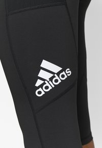Nära bild av svarta Adidas leggings med vitt logotyp på låret, synlig sömnad och meshpanel.