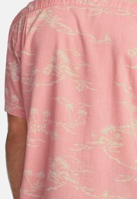 Kurzarmhemd aus leichtem rosa Stoff mit einem cremefarbenen tropischen Landschaftsmuster, das Palmen, Segelboote und florale Akzente zeigt.