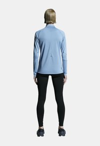 Hellblaues langärmliges Sportoberteil mit hohem Kragen, kombiniert mit schwarzen Leggings. Das Oberteil hat eine glatte Textur und eine figurbetonte Passform.