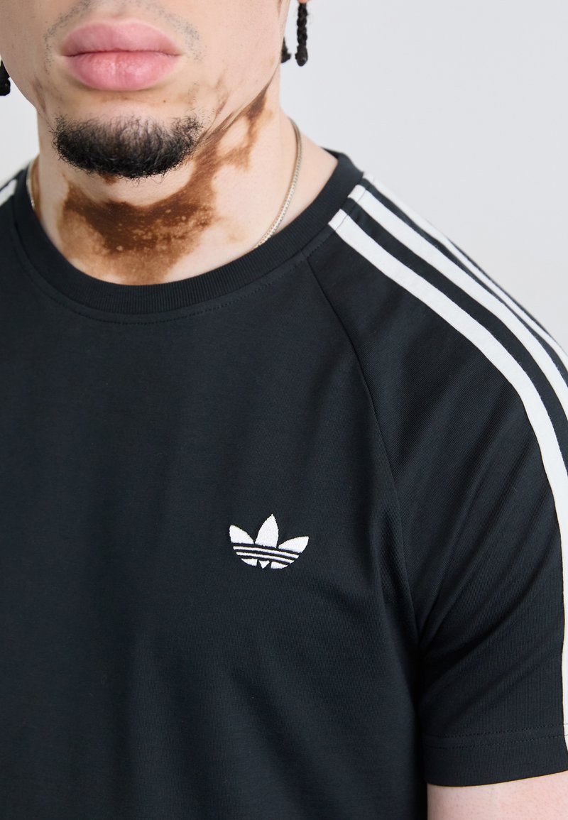 Schwarzes Baumwoll-T-Shirt mit weißem Adidas-Logo und drei weißen Streifen an den Schultern. Kurze Ärmel und Rundhalsausschnitt.
