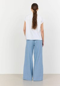 Camicia bianca a maniche corte abbinata a pantaloni larghi azzurri chiari, caratterizzati da una texture morbida e una vestibilità rilassata. Design semplice e minimalista.