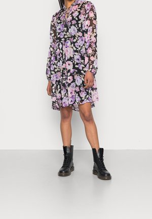 Kwiecista sukienka z długimi rękawami, wykonana z czarnej, przejrzystej tkaniny, zdobiona fioletowymi i różowymi kwiatami, zestawiona z czarnymi, sznurowanymi botkami typu combat.