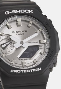 Montre G-SHOCK avec un bracelet en résine noire, un cadran argenté, un affichage analogique et numérique, des accents en acier inoxydable et une résistance à l'eau allant jusqu'à 20 bars.