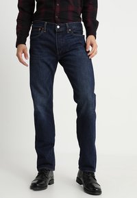 Jeans de mezclilla azul oscuro con un diseño de pierna recta, que cuentan con cinco bolsillos y costuras en contraste. Llevados con botas negras hasta el tobillo.